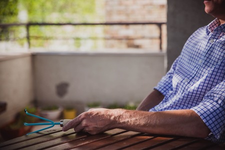 A man in a blue shirt is sitting at home on the balcony with a rake in his hands. He planted a salad. Favorite hobby. Close-upの写真素材