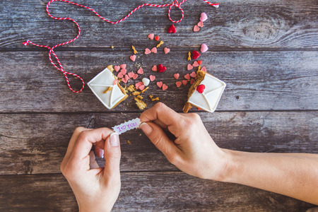 Baking Surprise Cookies with topping and icing on wooden background with pink heart. Woman holds a love letter. Top viewの写真素材