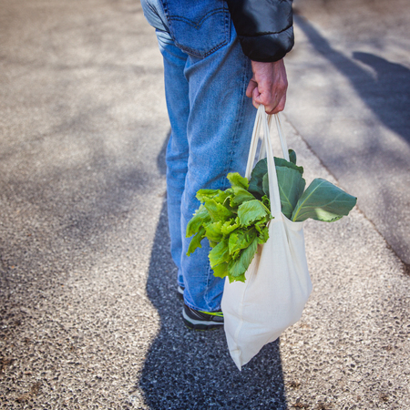 Fresh leaves in organic bag in man hand, healthy lifestyle. Shopping with eco shopper bag at street market, eco conceptの写真素材