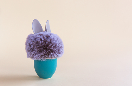 Fur ball with bunny rabbit ears in aquamarine egg stand on bright background. Easter minimal concept. Close-upの写真素材