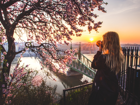 Woman taking photo the cityscape and the Liberty bridge over Danube from the terrace of the Gellert hill in Budapest, Hungary on sunriseの写真素材