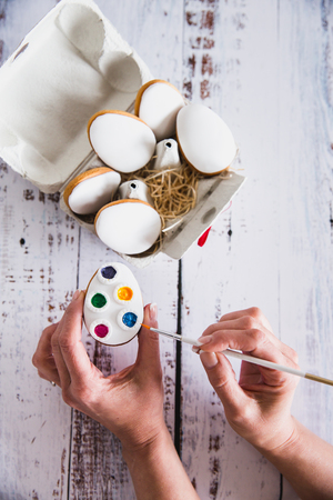 Hand decorating gingerbread colorful cookies on wooden background. Top View. Easter cookies.の写真素材