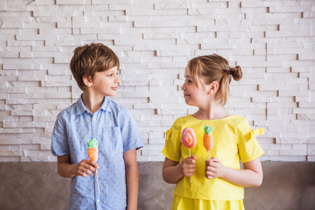 Adorable girl and boy holding colorful sweet meringues on a stick on Easter dayの写真素材