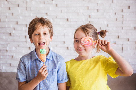 Adorable girl and boy holding colorful sweet meringues on a stick on Easter dayの写真素材