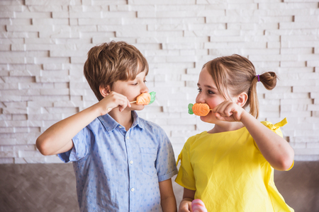 Adorable girl and boy holding colorful sweet meringues on a stick on Easter dayの写真素材