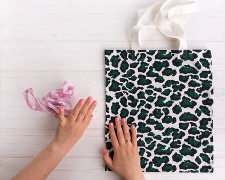 Womans hands choose eco shopping bag with trendy leopard pattern print against a plastic bag on white wooden background, Flat Lay. Save planet earthの写真素材