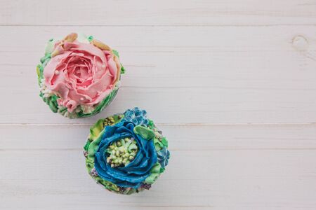 Two muffins with colored butter flowers on white wooden backgroundの写真素材