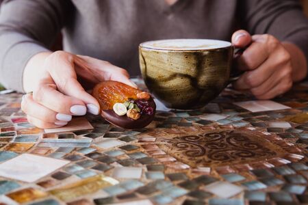 Woman hands hold a cup of cappuccino coffee on a colored glass table in cafeの写真素材