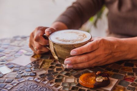 Woman hands hold a cup of cappuccino coffee on a colored glass table in cafeの写真素材