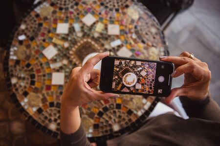 close-up hand holding phone mobile taking photo coffee on tableの写真素材