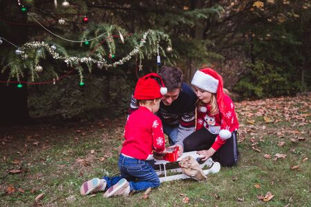 Father and two daughters open presents boxs near Christmas tree outdoor in the yard of the house.