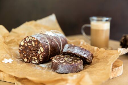 Homemade chocolate sausage on a wooden background. Dessert made of biscuits, chocolate and nuts is sliced on a wooden boardの写真素材