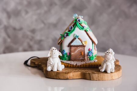 Homemade gingerbread house on wooden plate with two marzipan sheeps, close-up