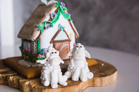 Homemade gingerbread house on wooden plate with two marzipan sheeps, close-upの写真素材