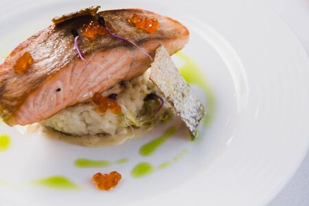 Gourmet roasted salmon steak baked in the oven, served on a pillow of risotto and red caviar as a...