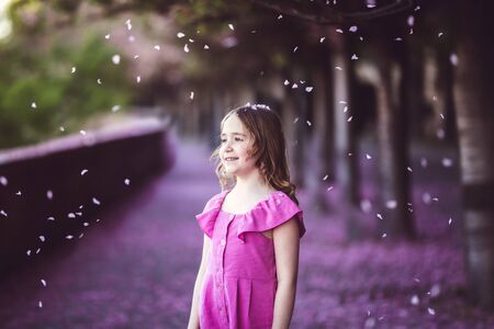 Beautiful girl in pink dress in cherry blossom park on a spring day, flower petals falling from the treeの写真素材