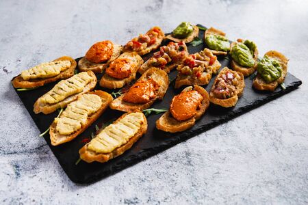 Assorted bruschetta with various toppings on a dark plate on white background. Appetizing bruschetta. Variety of small sandwiches.の写真素材