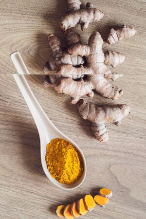 Raw organic orange turmeric root and powder in the spoon on wooden background. Indian oriental low...