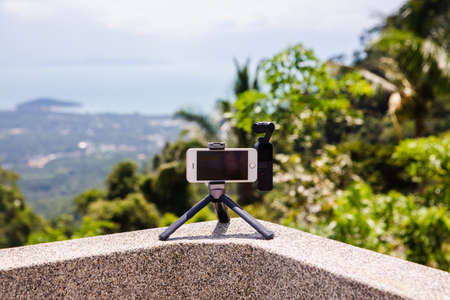 Koh Samui, Thailand - August 13, 2019: DJI Osmo Pocket connected with smartphone in tripod to take footage of panorama view on island with ocean and tree on background.のeditorial素材