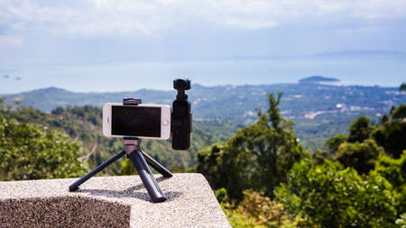 Koh Samui, Thailand - August 13, 2019: DJI Osmo Pocket connected with smartphone in tripod to take footage of panorama view on island with ocean and tree on background.のeditorial素材