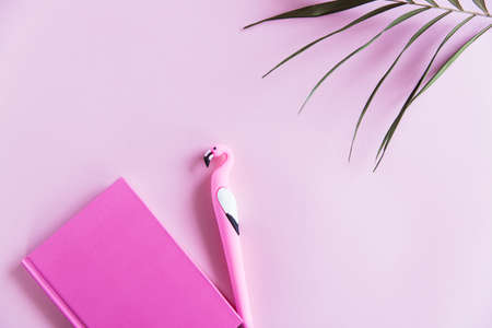 Pink notebook for notes, funny flamingo pen and green palm leaves on pink pastel background. Flat lay. Top view. Copy spaceの写真素材