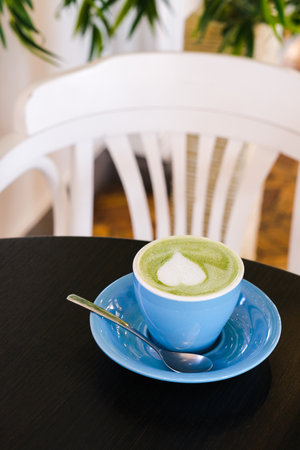 Matcha green latte in blue cup on a black table with white chair on background. Vertical photo taken in cafeの写真素材