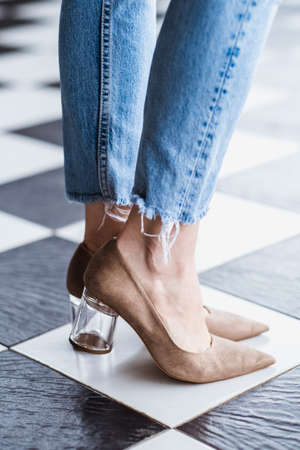 Beautiful slim and slender female legs in jeans in beige high heels. Womans legs on a checkerboard...