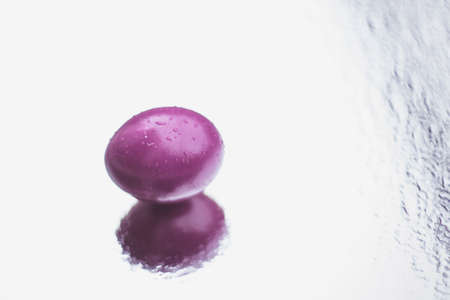 Chicken colored egg with drops of water on the surface on a mirror background