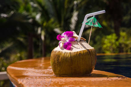Fresh cold coconut with cocktail straw near the pool