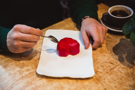 Red cake in the shape of a heart is on the table. Mans hands with spoons stretch into a pie. Valentines Dayの写真素材