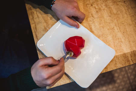 Red cake in the shape of a heart is on the table. Mans hands with spoons stretch into a pie....