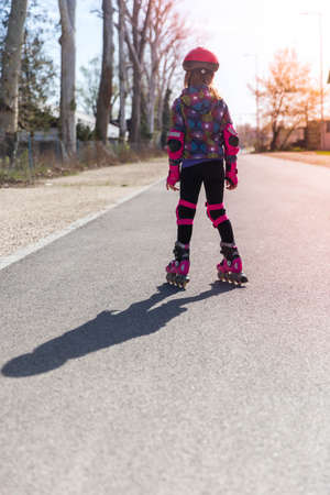 Little girl in pink roller skates and protective equipment outdoors on the road