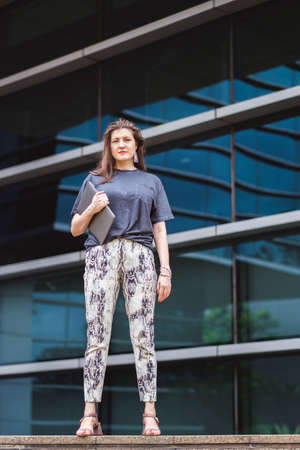 Portrait of brown long hair pretty woman or businesswoman in smart casual with notebook outdoors with office buildings in the backgroundの写真素材