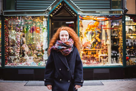 Red hair girl enjoying European Christmas Market. Blurred Lights and colored toys in Christmas store on backgroundの写真素材