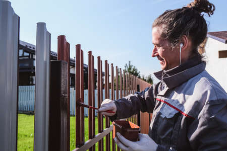 A man paints an iron fence in the garden and listens music in headphone.の写真素材