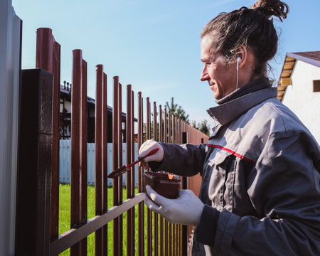 A man paints an iron fence in the garden and listens music in headphone.の写真素材