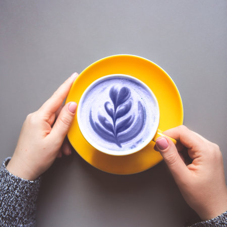 Woman holding yellow hot trendy purple latte with art flower petals on the foam on grey wooden table backgroundの写真素材