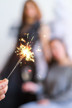 Woman hand with sparkler with group of friends having fun on background unfocused.の写真素材