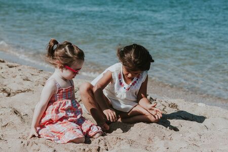 Two daughters play with sand on the beachの写真素材