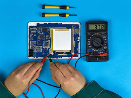 Technician or engineer repairs the digital Board and performs a multimeter test. Top view on a blue...