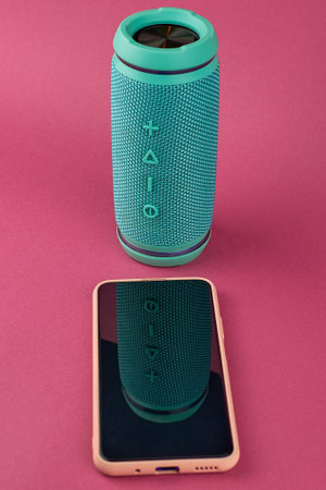 Turquoise portable audio speaker and pink phone. Wireless speaker and smartphone on a pink...