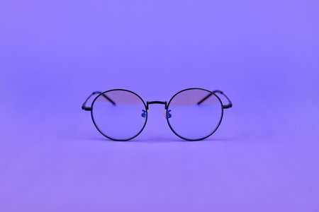 Glasses with a blue light filter to protect the eyes while working at the computer. Round glasses for filtering blue light. Stylish round lenses on a purple background, top viewの写真素材