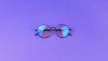 Glasses with a blue light filter to protect the eyes while working at the computer. Round glasses for filtering blue light. Stylish round glasses on a purple background, top viewの写真素材