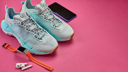 Running shoes, a phone, a smart watch and wireless headphones. Sports accessories for running on a...