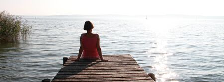 Woman is sitting by the water on a footbridgeの写真素材