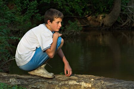 Teenage boy crossing river on a logの写真素材