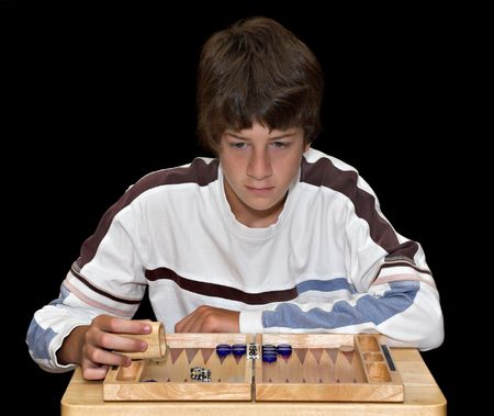 A young teenage boy playing a game of backgammon. The boy and board are isolated over a black...