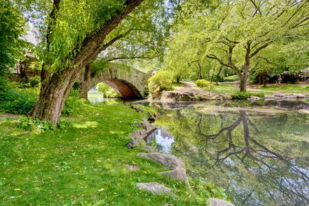 A stone bridge in Central Park, NY. There is a large tree and reflection in the pond that runs under the bridge.の写真素材