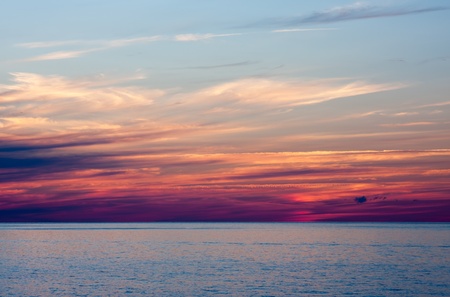 An Evening Sunset Over Water. The sky is blue at the top and purple closer to the waterの写真素材