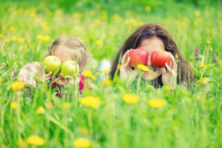 Mother and daughter lying on green meadow and holding applesの写真素材
